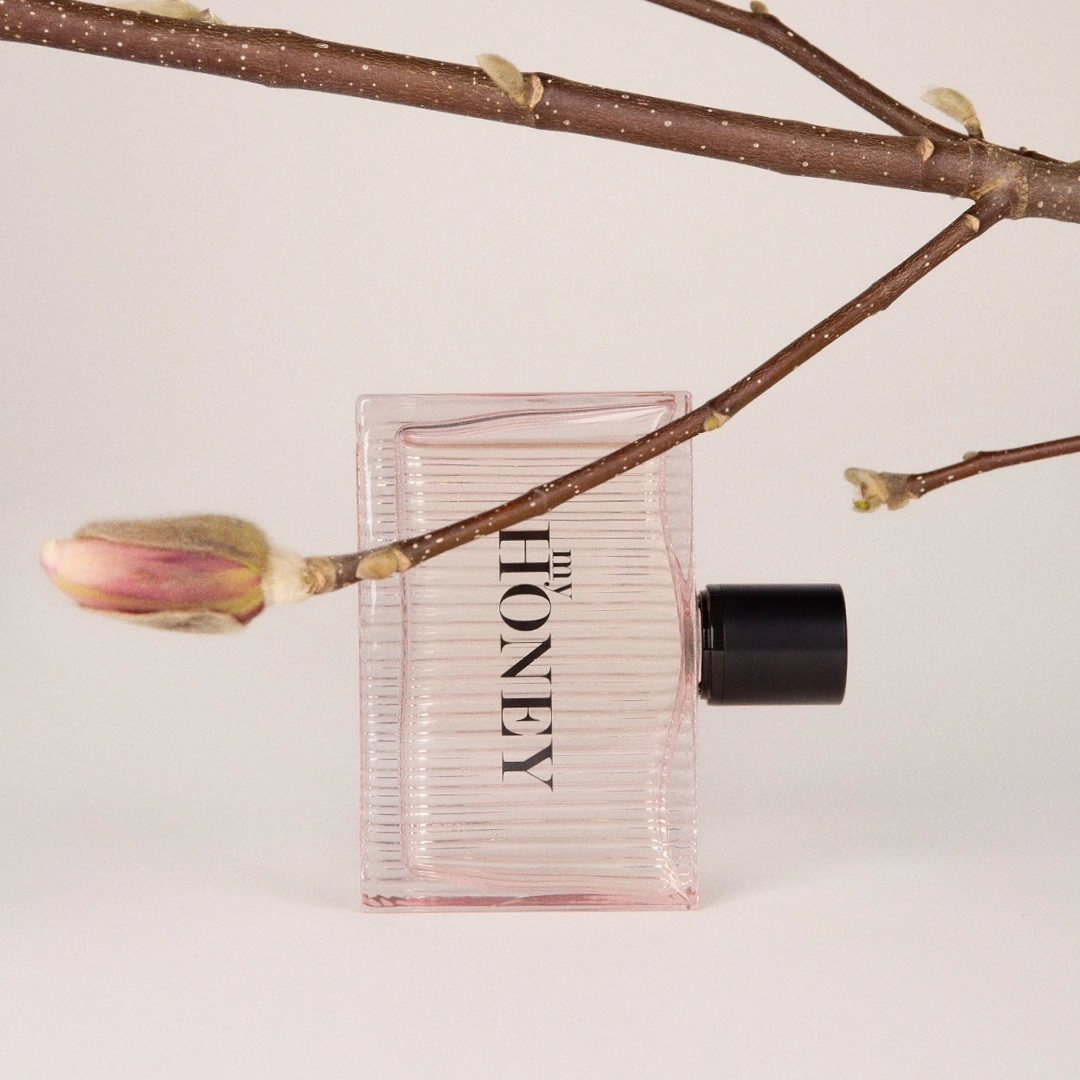 Perfume bottle with branch and bud, light background, product photography
