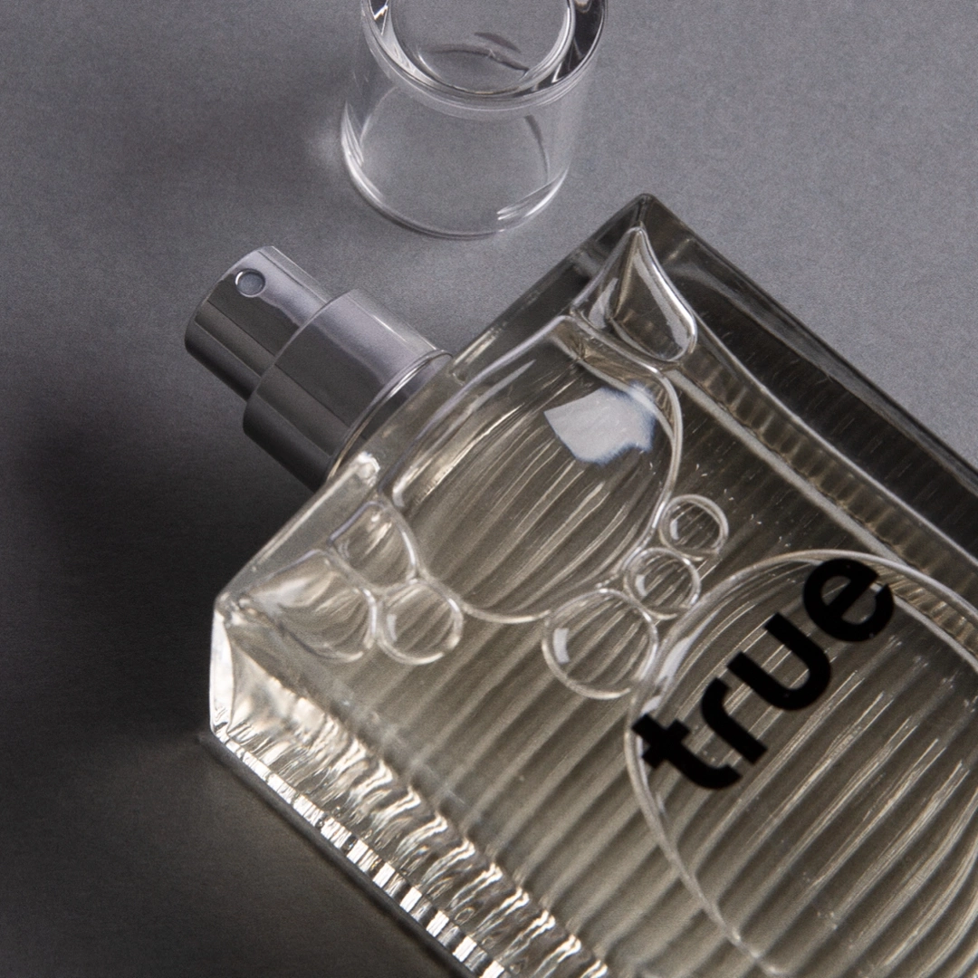 Parfümflasche mit der Aufschrift "true" auf grauem Hintergrund, Nahaufnahme.