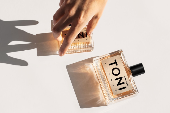 Two perfume bottles with shadows and a hand holding one of them.