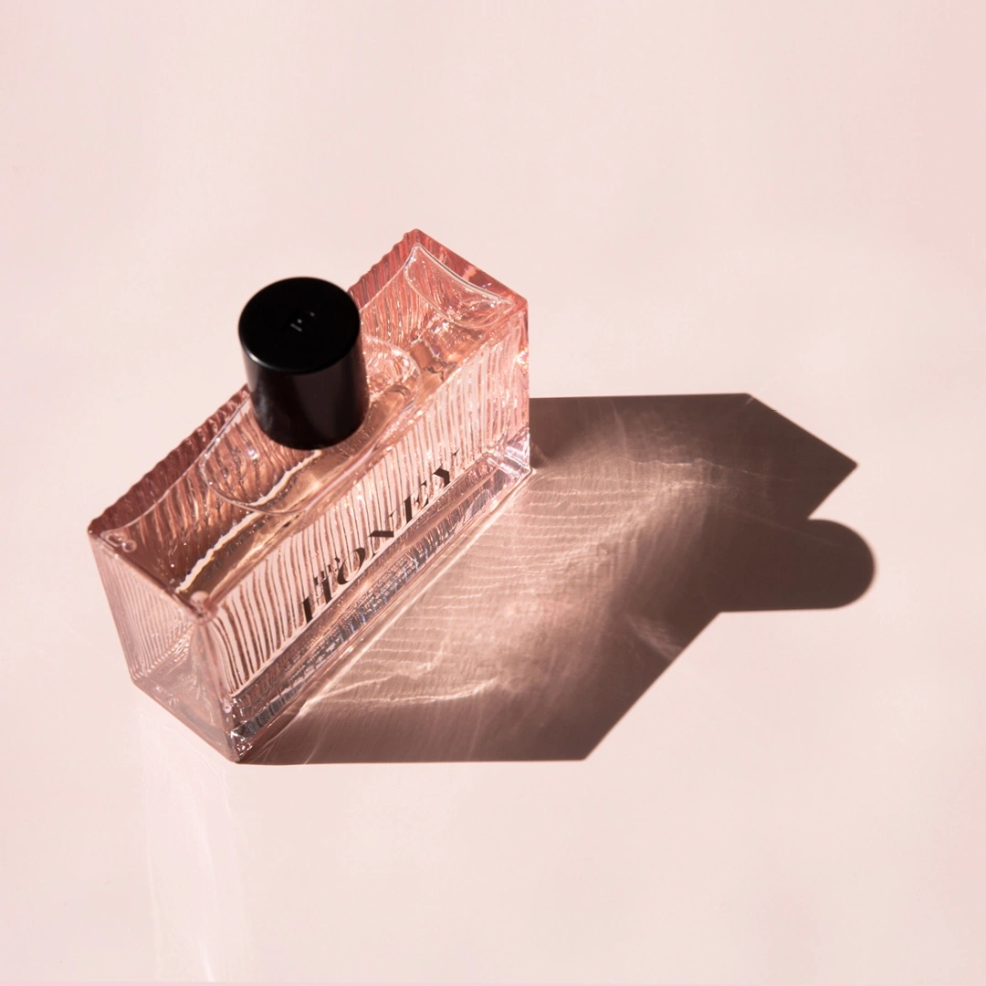 Perfume bottle on pink surface with shadow, Honey lettering visible