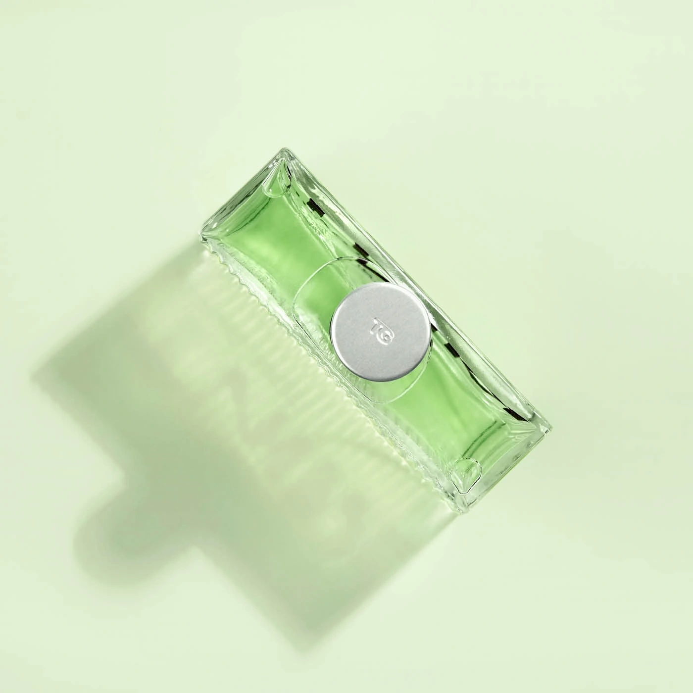 Green perfume bottle on light green background, with shadow, minimalist