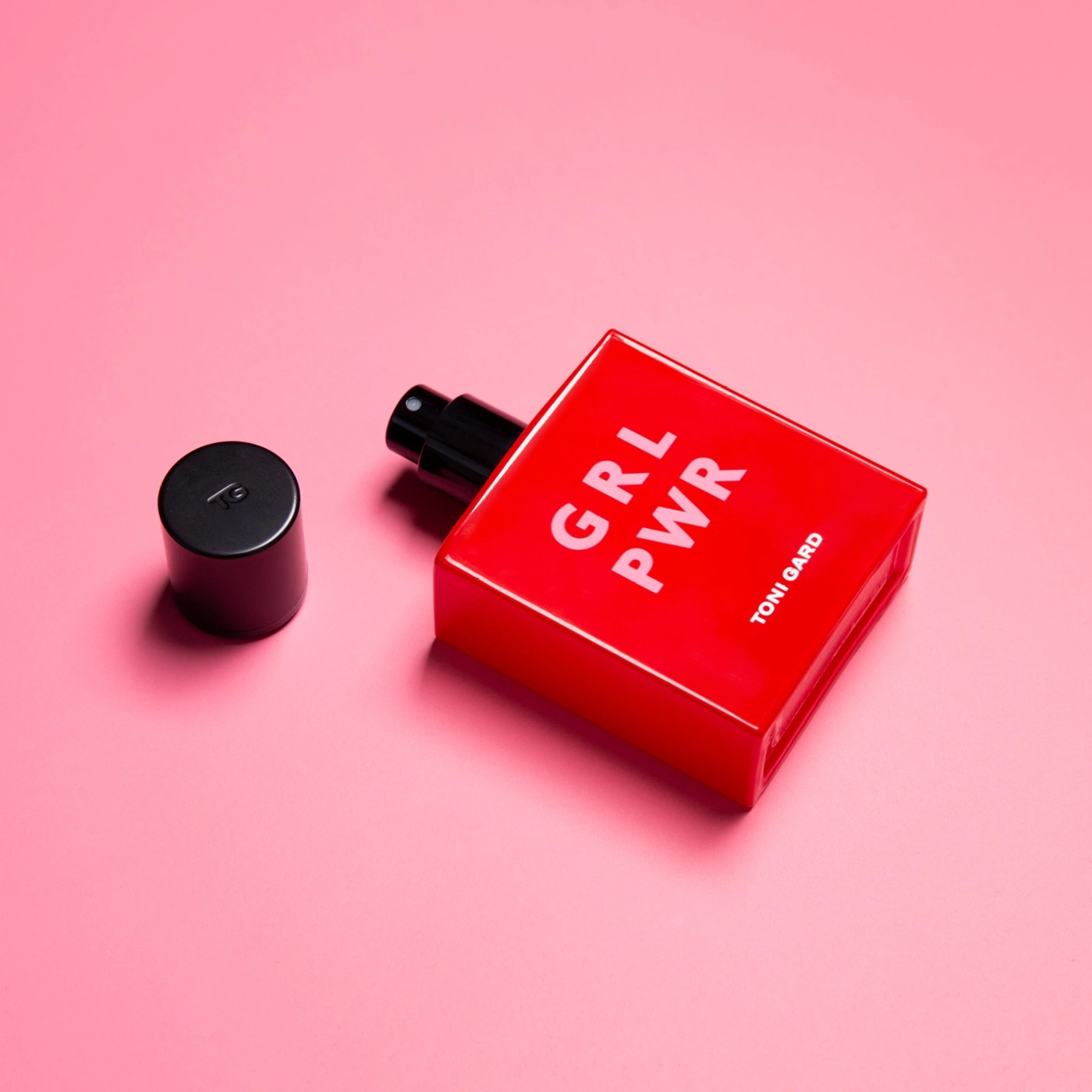 Rote Parfümflasche mit GRL PWR-Aufdruck auf rosa Hintergrund.