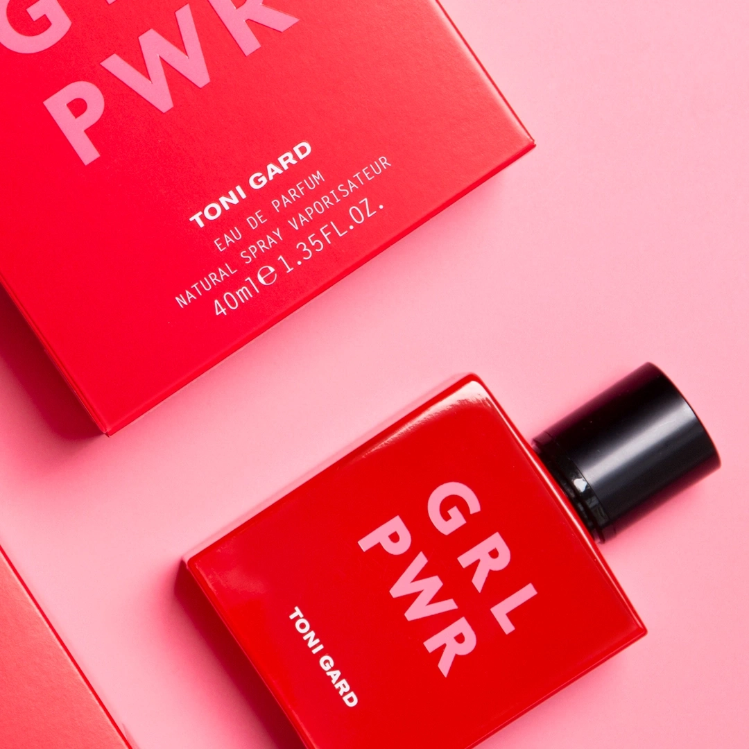 Rotes Parfüm mit GRL PWR-Aufdruck und TONI GARD-Logo auf rosa Hintergrund.