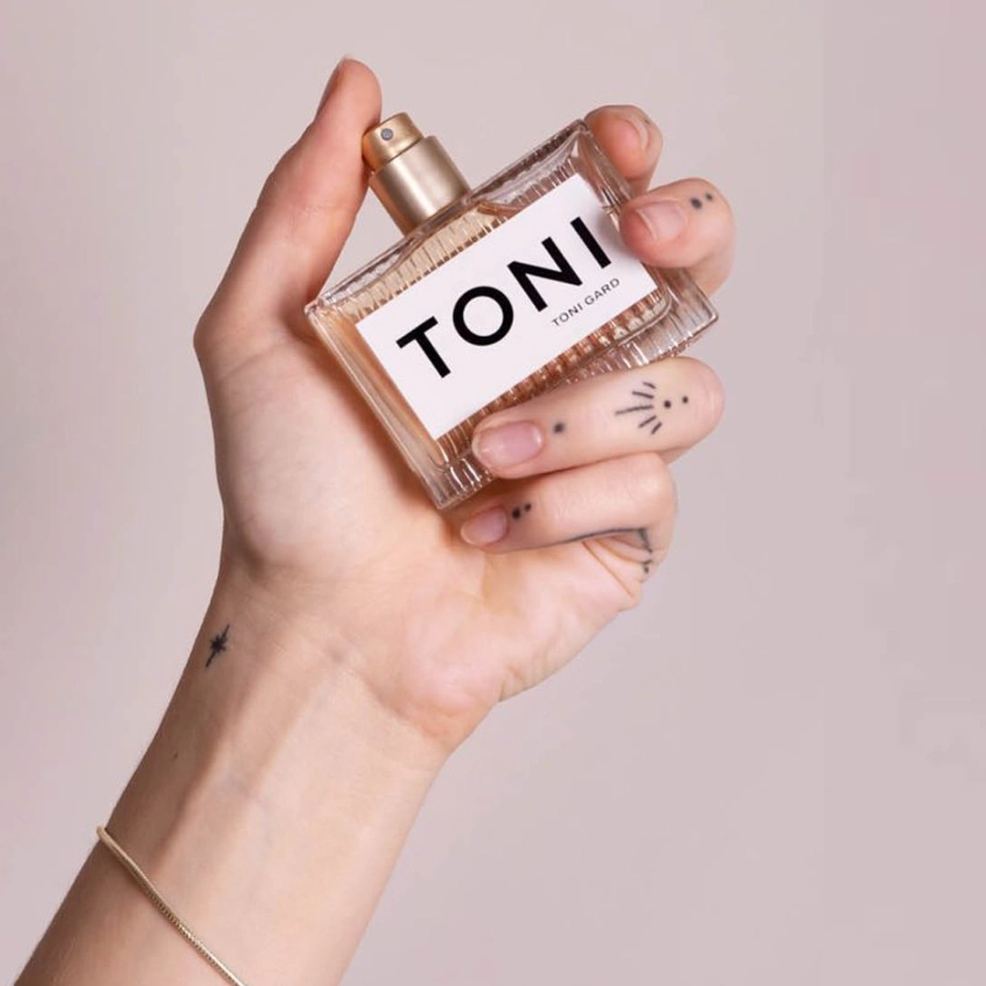 Hand hält Parfümflasche mit dem Schriftzug TONI, Tattoo, Armband, rosa Hintergrund